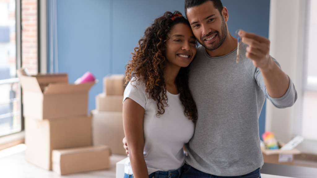 A couple is looking at their house keys inside their new assumable mortgage home with packing boxes in the background.  