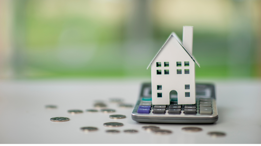 A toy house sits on top of a calculator and change for FHA assumable mortgage education.