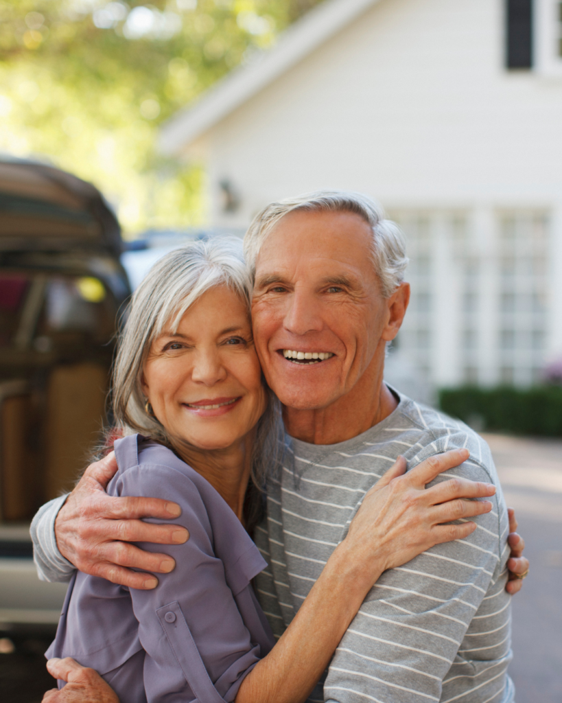 A picture of an older couple smiling and hugging as they just moved into their new home.